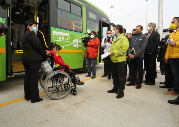 A group including a woman in a wheelchair near an electric bus
