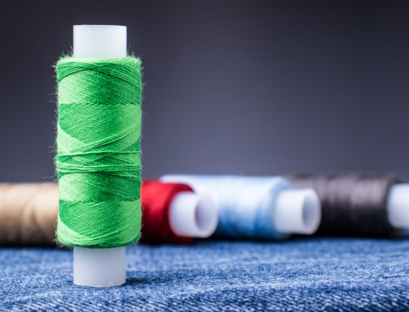 Spool of green thread in the foreground with other spools of thread behind it